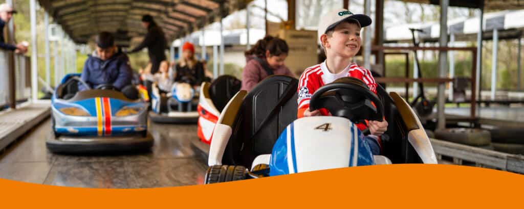Mehrere Personen fahren in Autoscootern auf einer Fahrbahn mit grauem Boden.