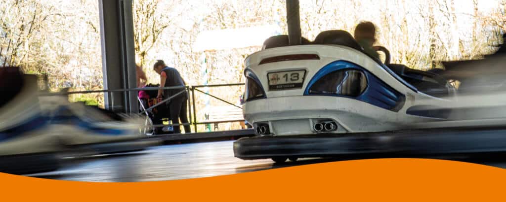 Mehrere Personen fahren in Autoscootern auf einer Fahrbahn mit grauem Boden.