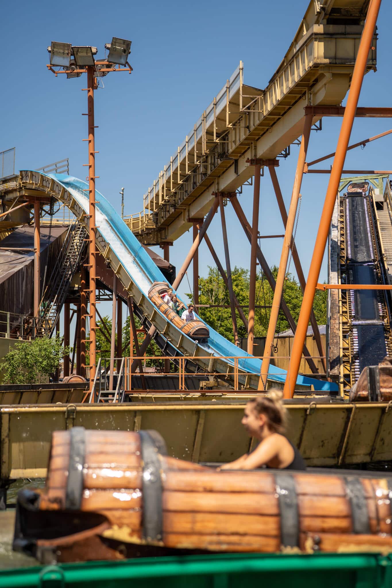 Besucher fahren in einem fassförmigen Boot eine blaue Wasserrutsche in einem Freizeitpark hinunter