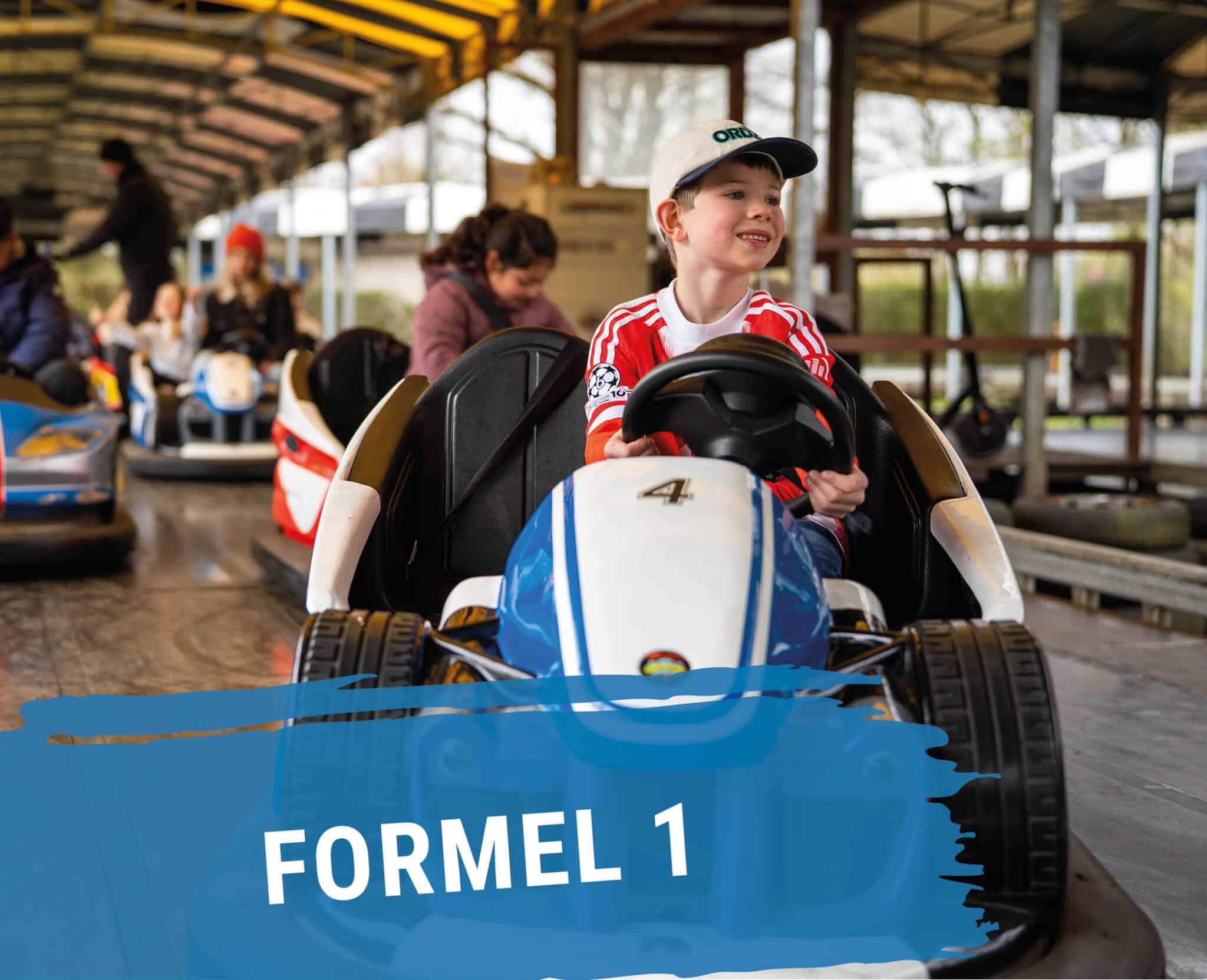 Mehrere Personen fahren in Formel 1 Autos auf einer Fahrbahn mit grauem Boden.
