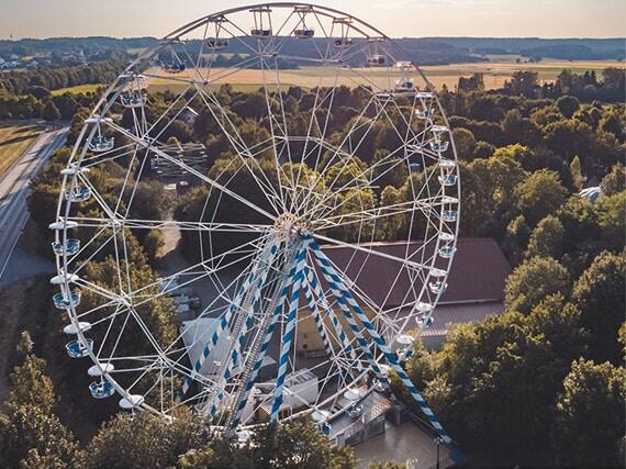 Ein großes Riesenrad mit blauen und weißen Elementen in einem Parkgebiet mit Bäumen im Hintergrund.