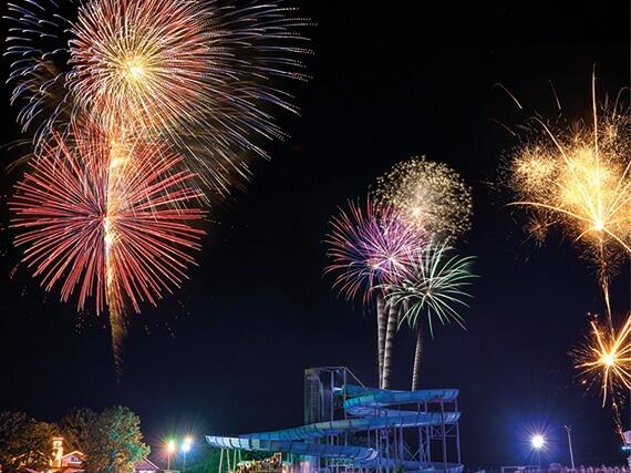 Buntes Feuerwerk über einer Wasserrutsche bei Nacht mit verschiedenen Farben und Formen.
