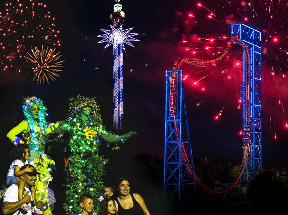 Im Skyline Park bei Nacht leuchten Feuerwerk, ein hoher Turm und eine beleuchtete Achterbahn über kostümierten Performern.
