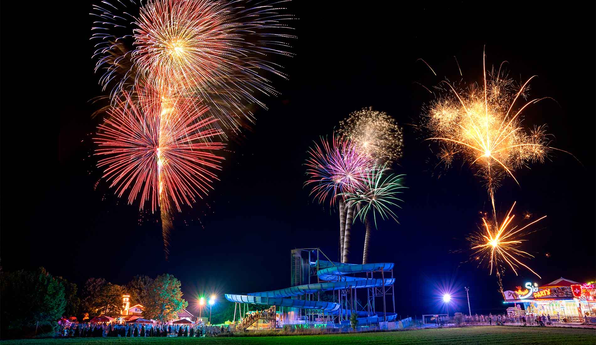 Buntes Feuerwerk über einem Wasserpark mit einer Wasserrutsche bei Nacht.