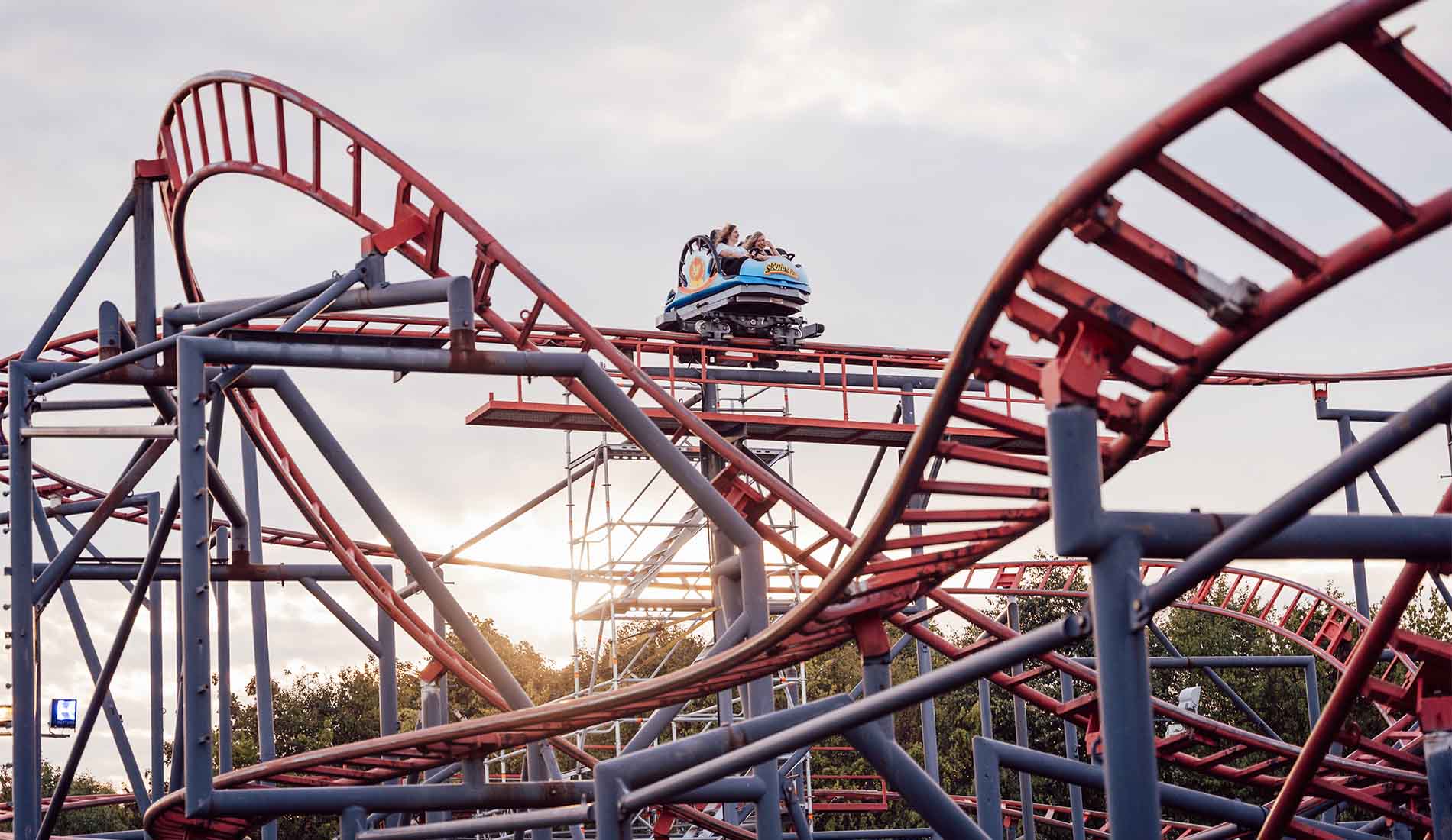 Achterbahn mit Fahrgästen auf der Strecke im Skyline Park während der Dämmerung.