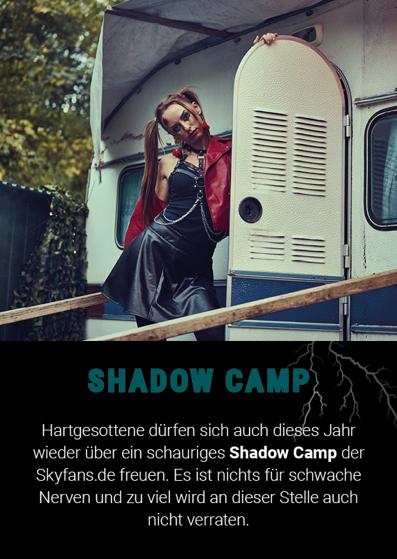 Frau in schwarzem Outfit mit rotem Akzent steht vor einem Wohnwagen im Schatten-Camp.