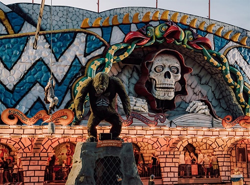 Fassade einer Geisterbahn mit einem großen Totenkopf und einer Statue eines Monsters im Allgäu Skyline Park.