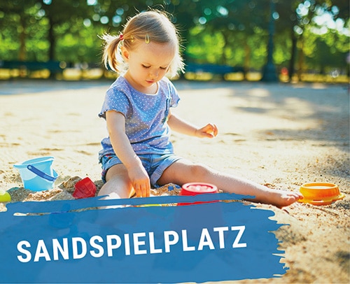 Ein Kind sitzt im Sand und spielt mit Spielzeug am Sandspielplatz.