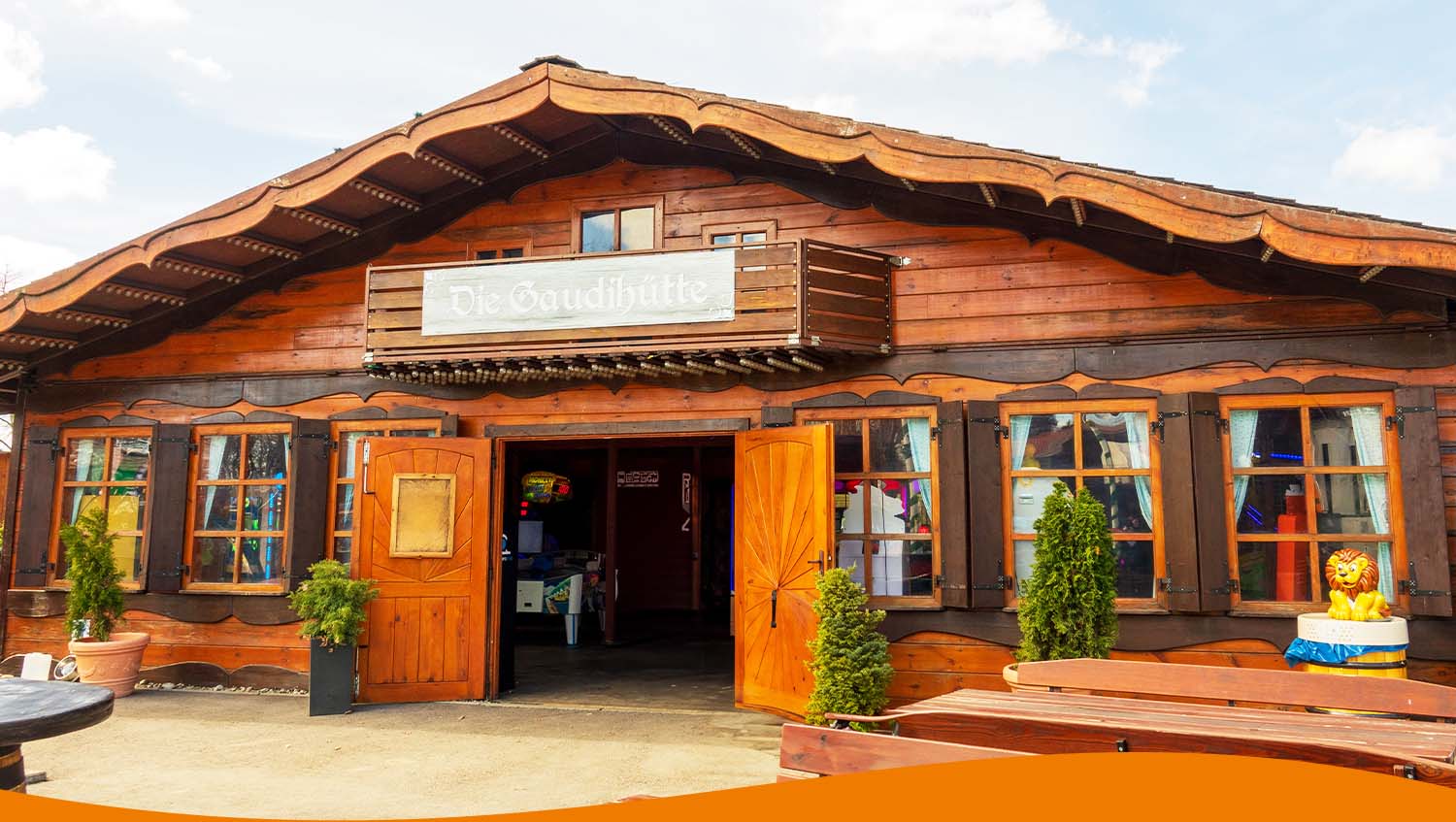 Holzhütte mit einem Schild, das 'Die Gaudihütte' anzeigt, und offenen Türen.