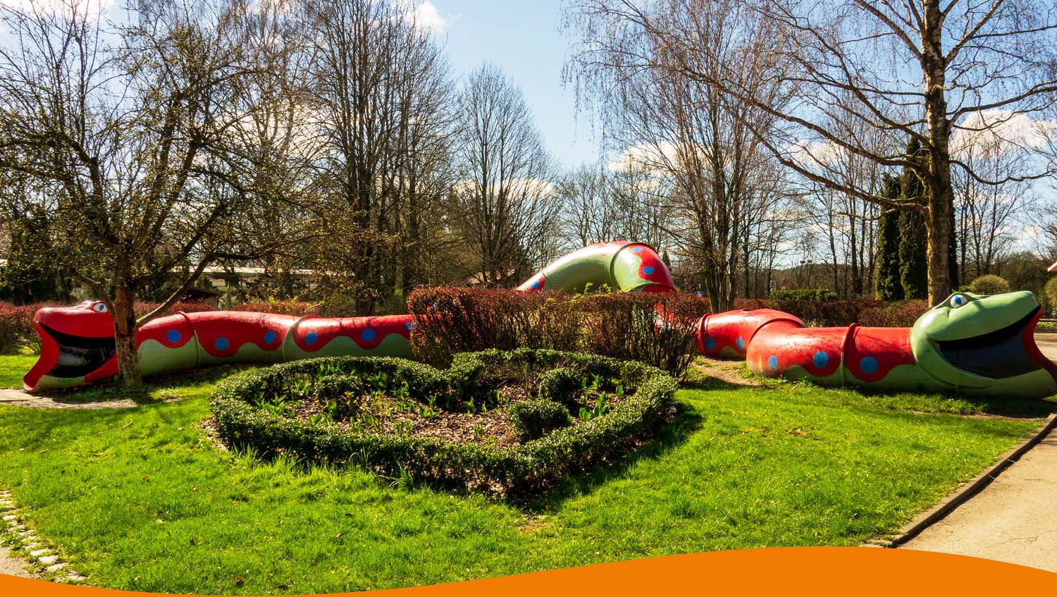 Bunte Schlangenröhre mit roten und grünen Elementen in einem Gartenbereich.