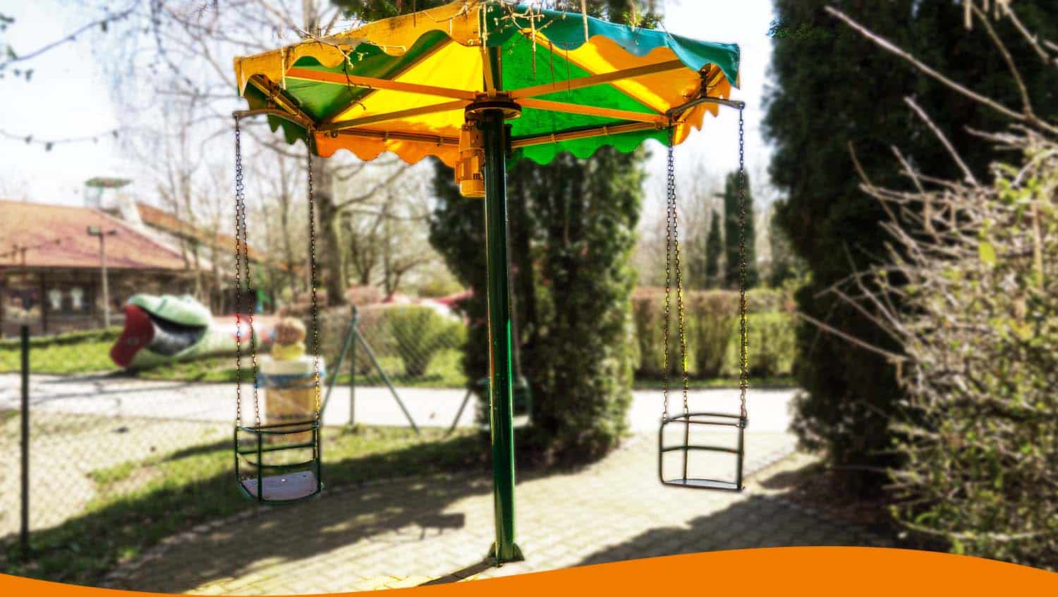 Kettenflieger Spielgerät mit gelb-grünem Dach und zwei Schaukeln in einem Spielplatzbereich.