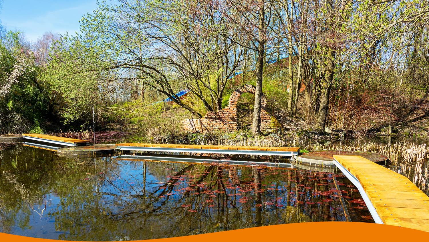 Holzstege über dem Wasser des Lago Fontana mit umliegender Vegetation und einem alten Steinbogen.