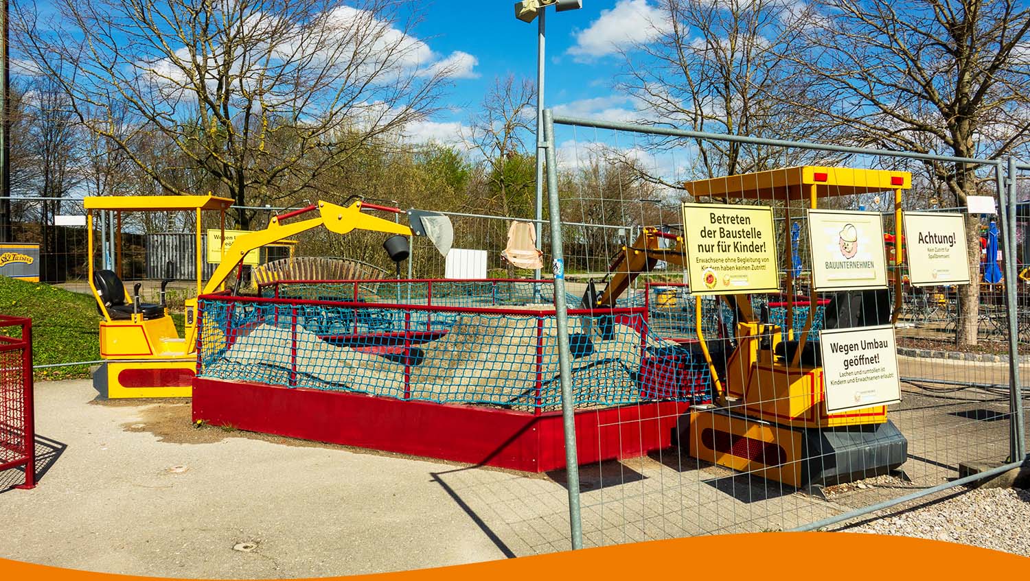 Ein Spielplatz mit einem Bagger für Kinder, umgeben von einem Sicherheitszaun.