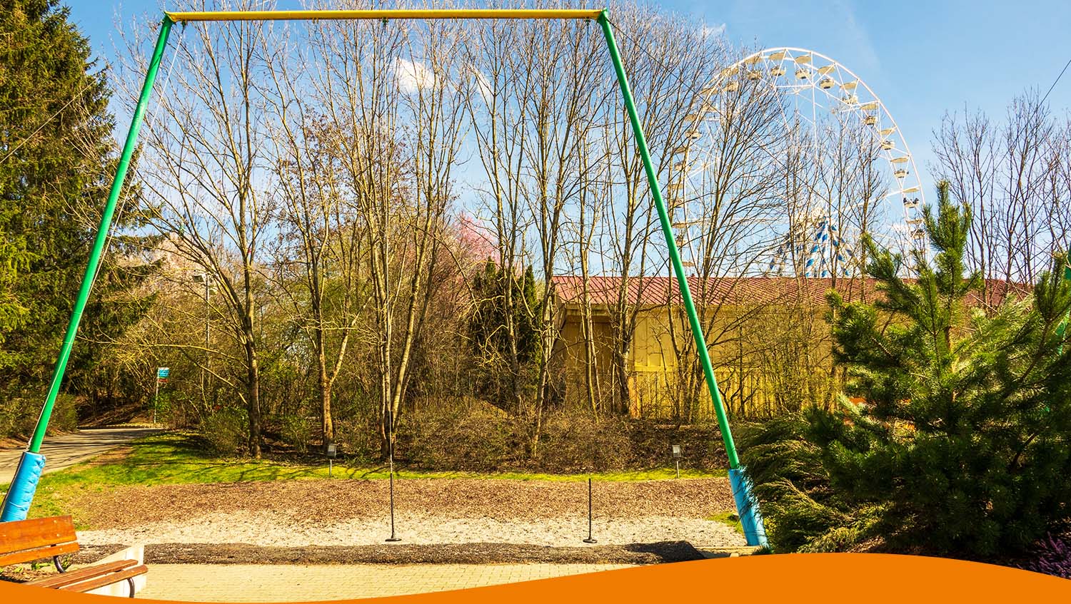 Eine Schaukel in einem Park mit Bäumen und einem Riesenrad im Hintergrund.