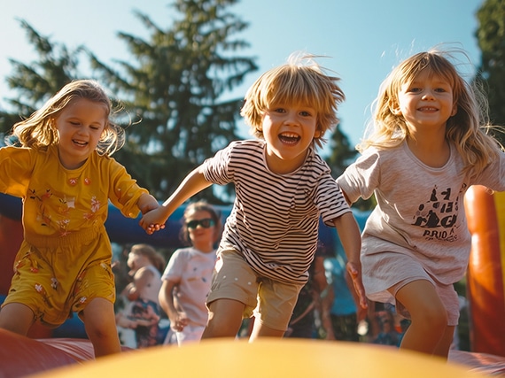 Drei Kinder, die fröhlich auf einer Hüpfburg spielen und lachen.