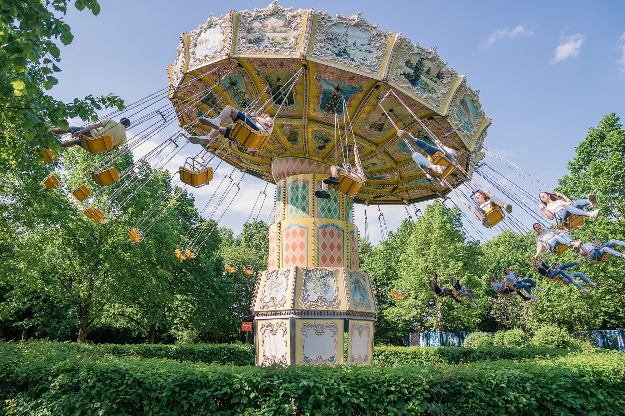 Wellenflieger Fahrgeschäft mit schwingenden Sitzen in einem Freizeitpark unter blauem Himmel.