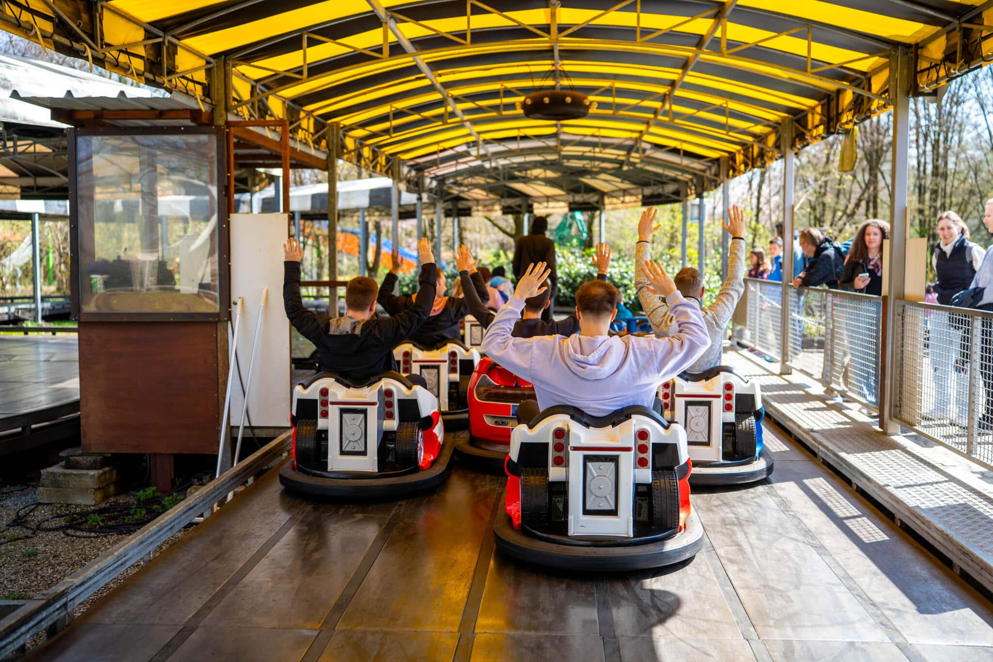 Besucher mit erhobenen Händen fahren in Fahrzeugwagen einer überdachten Achterbahn in einem Freizeitpark