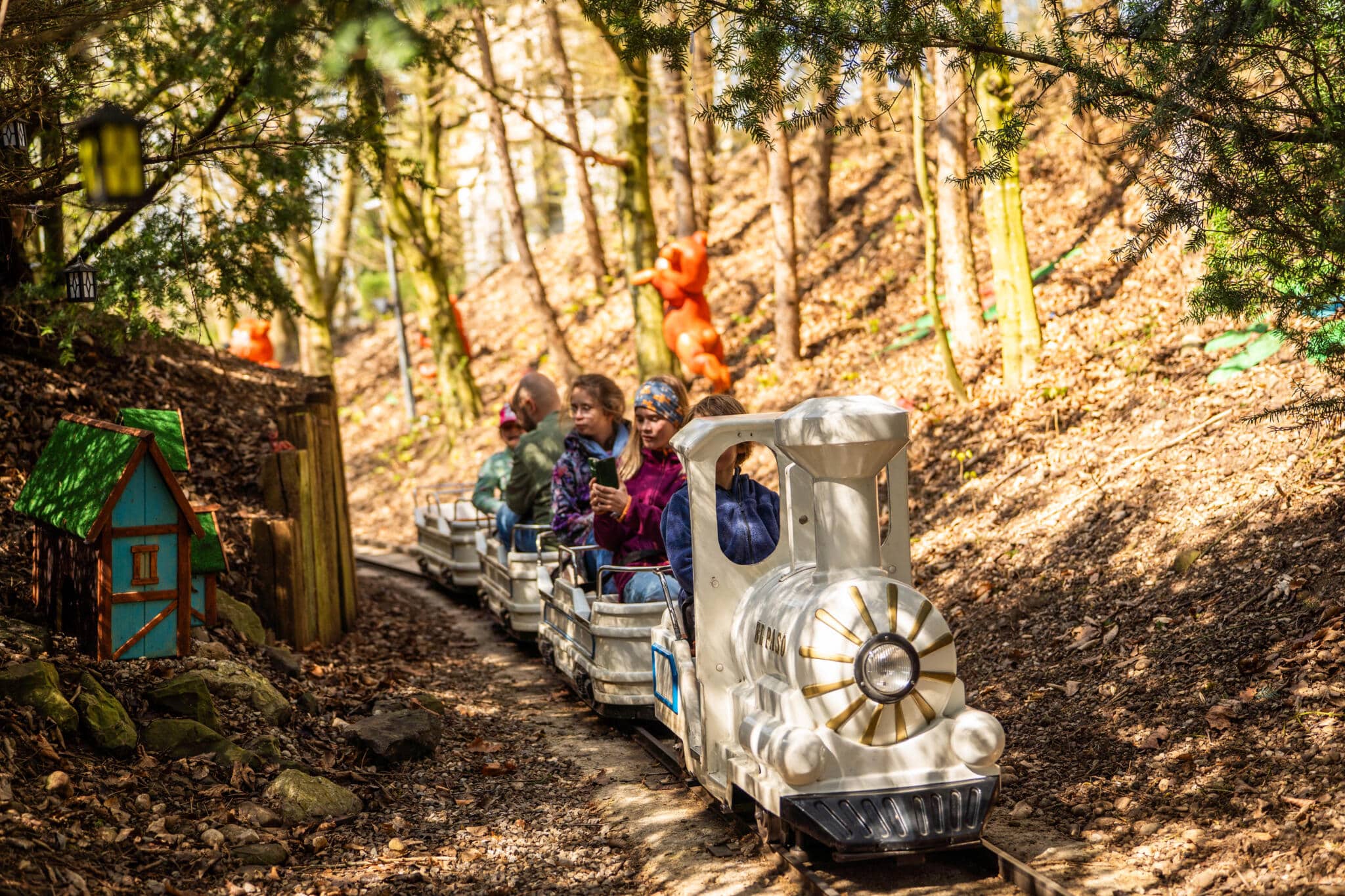 Kinder fahren mit einer kleinen weißen Liliputbahn durch einen märchenhaften Wald mit bunten Figuren