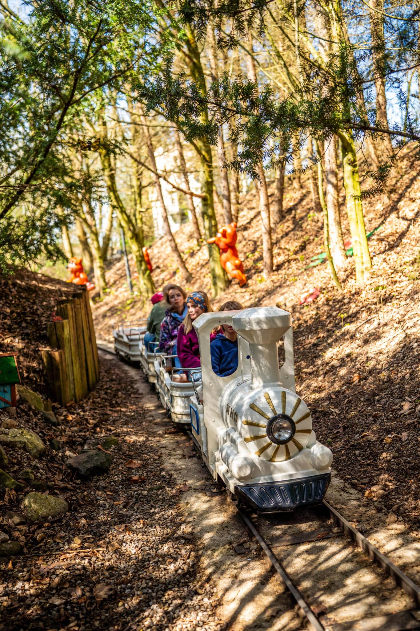 Kinder fahren mit einer kleinen weißen Liliputbahn durch einen märchenhaften Wald mit bunten Figuren