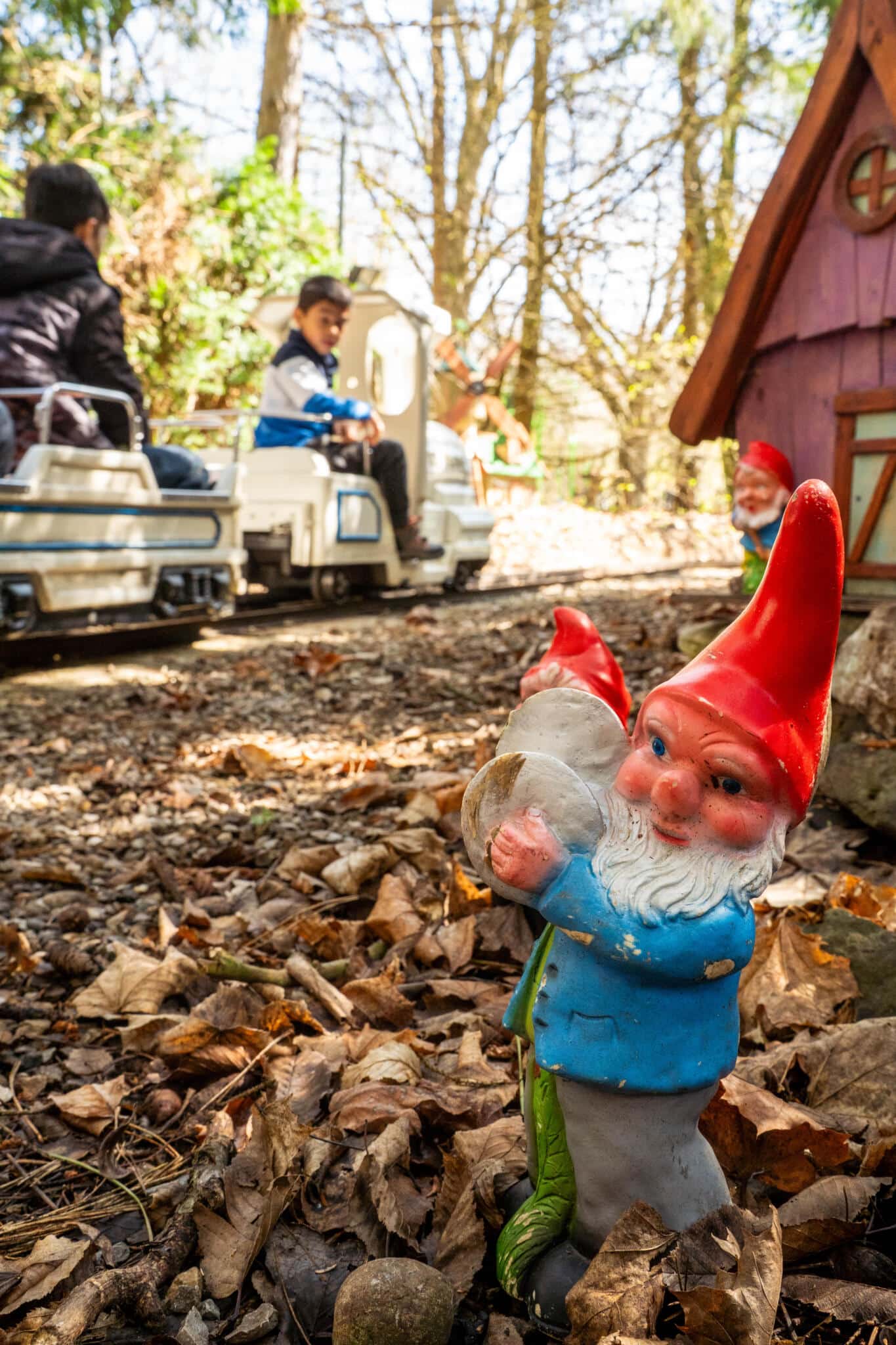 Gartenzwerg mit roter Mütze im Vordergrund, im Hintergrund fahren Kinder mit einer Minibahn durch einen Freizeitpark