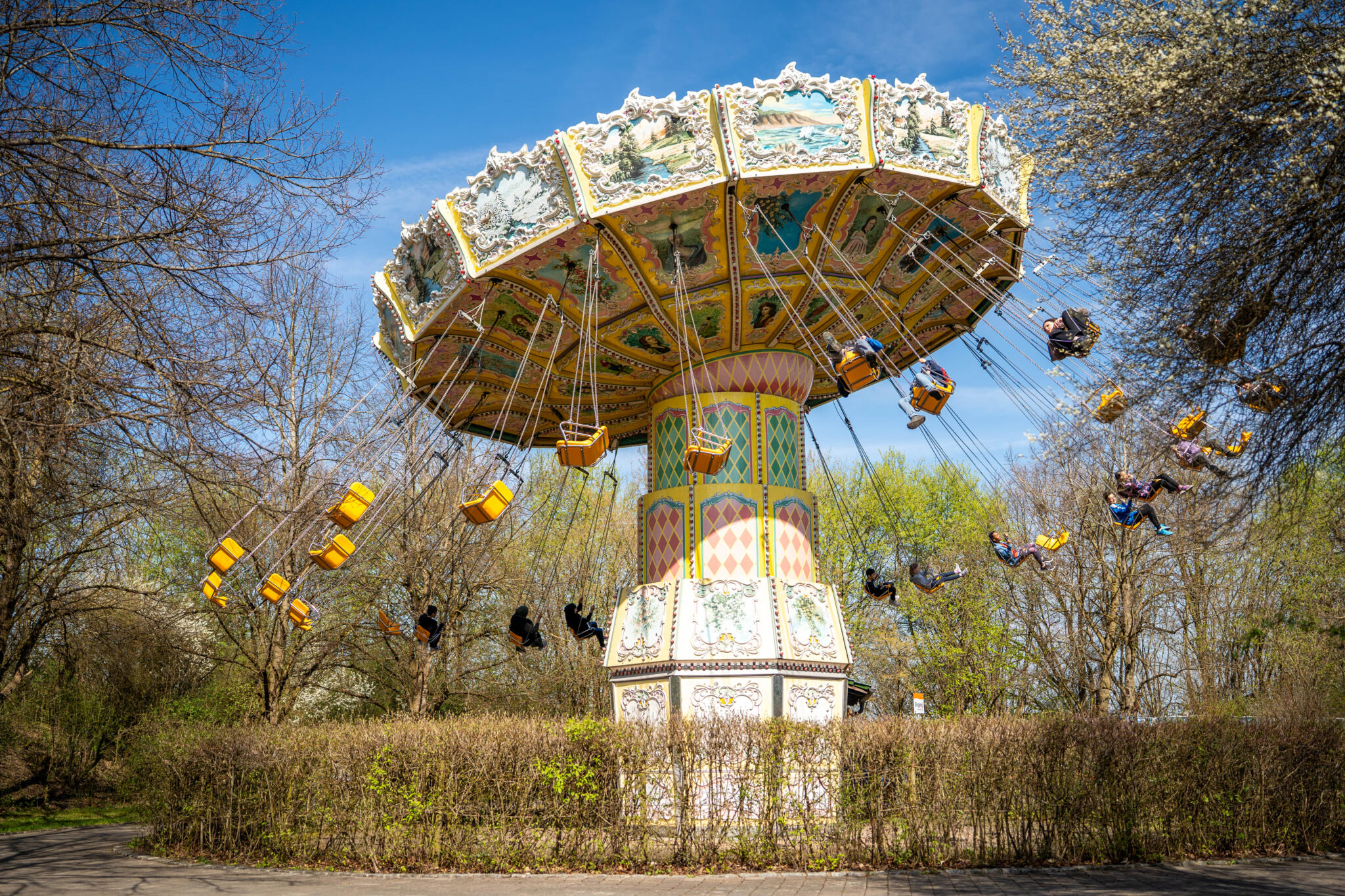Wellenflieger Fahrgeschäft mit schwingenden Sitzen in einem Freizeitpark unter blauem Himmel.