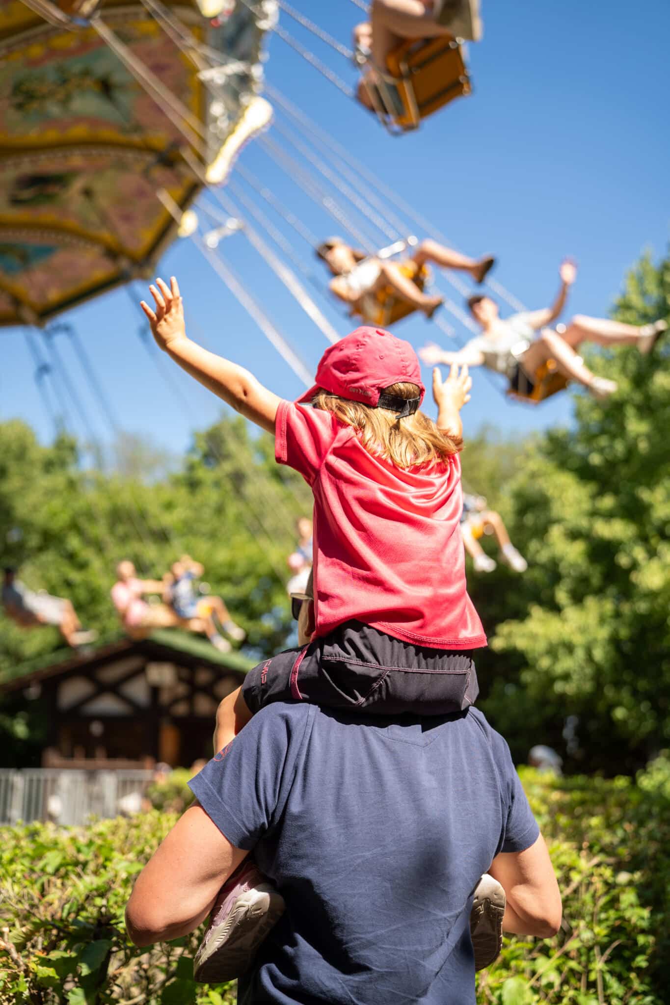 Wellenflieger Fahrgeschäft mit schwingenden Sitzen in einem Freizeitpark unter blauem Himmel.