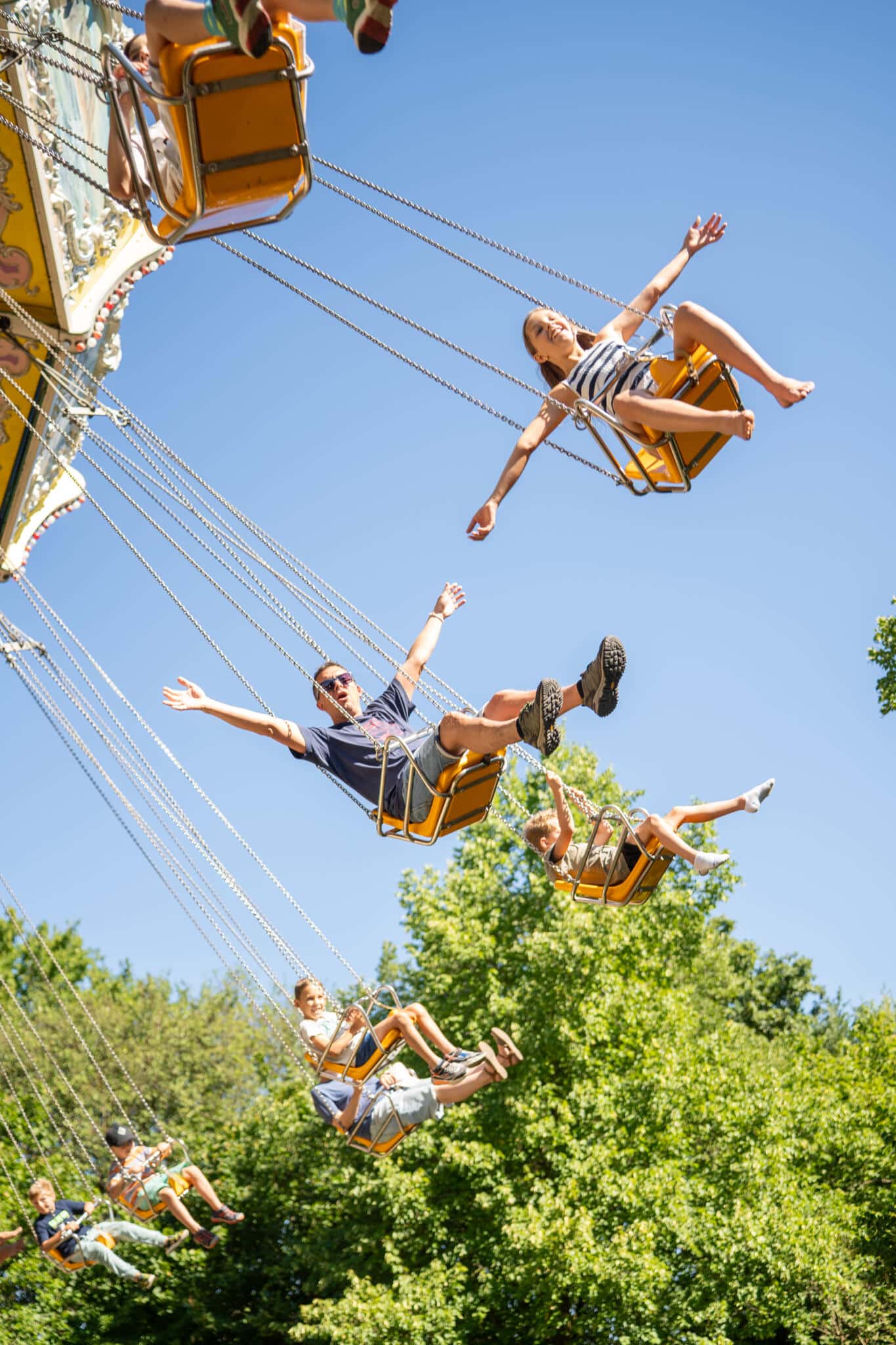 Wellenflieger Fahrgeschäft mit schwingenden Sitzen in einem Freizeitpark unter blauem Himmel.