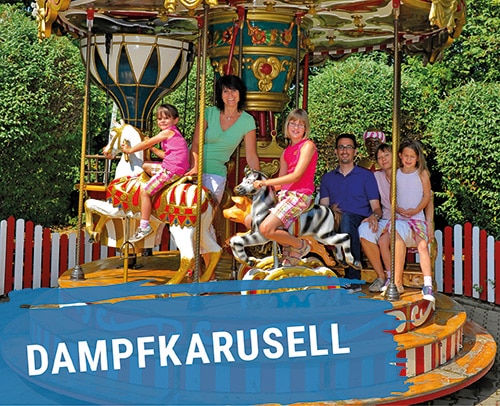 Dampfkarussell mit mehreren Personen, die auf bunten Pferden sitzen.