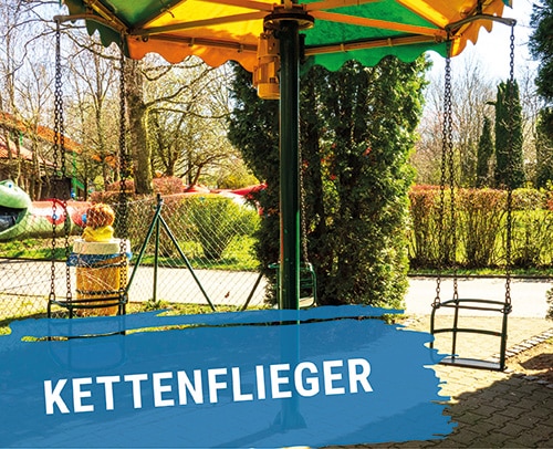 Kettenflieger Spielgerät mit buntem Dach und hängenden Sitzen in einem Freizeitpark.