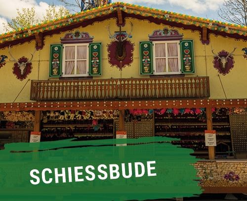Bunte Schiessbude mit dekorativen Elementen und Fenstern auf einem Festplatz.
