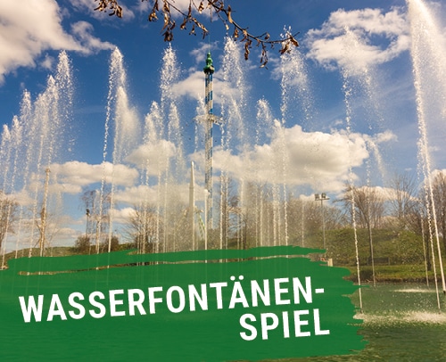 Sprudelnde Wasserfontänen in einem Park mit blauem Himmel und Wolken.