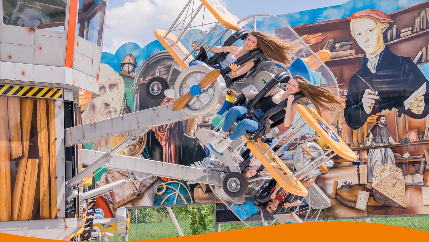 Zwei Personen in einem Flugzeugkarussell mit sich drehenden Sitzen und einem bunten Hintergrund.